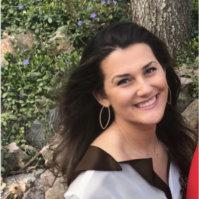A white woman with dark hair and hoop earrings smiles broadly