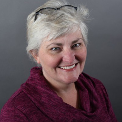 A smiling white woman with short salt-and-pepper hair and black reading glasses on top of her head