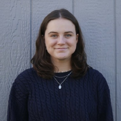A white woman with dark brown, should-length hair and wearing a navy cable knit sweater smiles