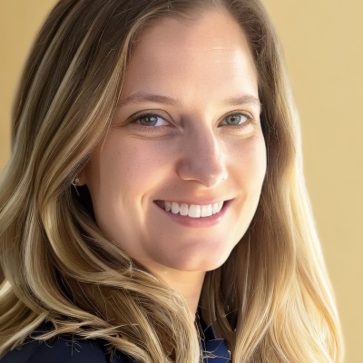 A white woman with wavy dark blonde hair and wearing a dark blue shirt smiles